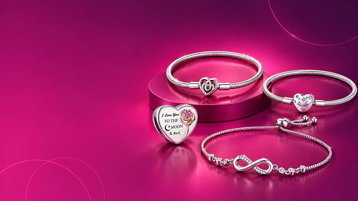 Four silver-toned bracelets and a heart-shaped charm with engraved text and a rose motif, arranged on a glossy pink and magenta studio background.