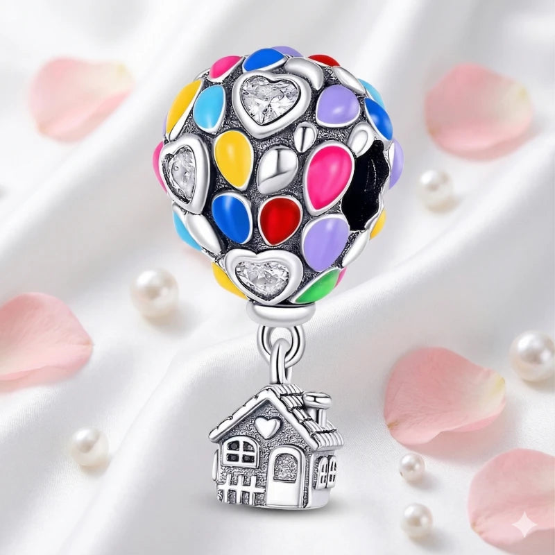 Colorful heart-shaped charm with a house pendant on a white background with pink petals.