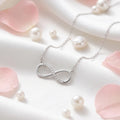 Silver infinity necklace on a soft pink background with pearls