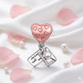 Heart-shaped charm with pink hearts and a pearl on a white background with pink petals and pearls.