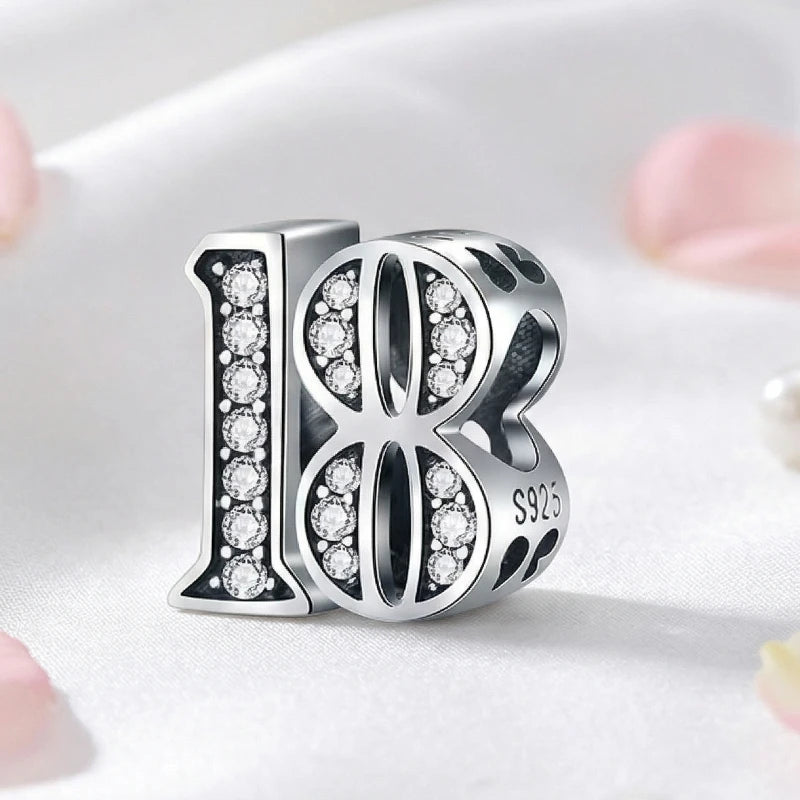 Silver charm with the number 18 and embedded stones on a light background