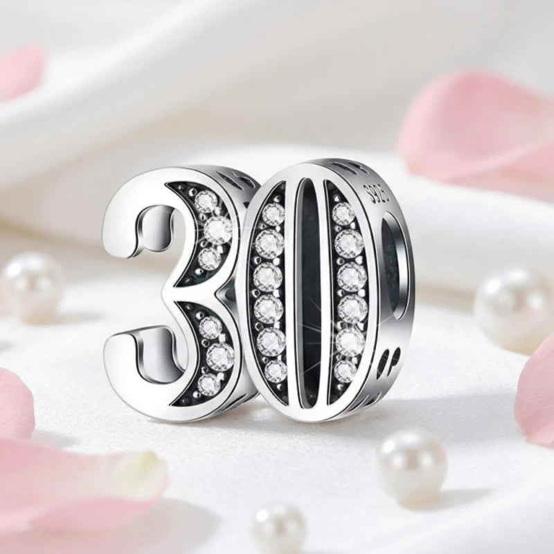 Silver charm with '30' and sparkling stones on a soft background with pink flowers and pearls.